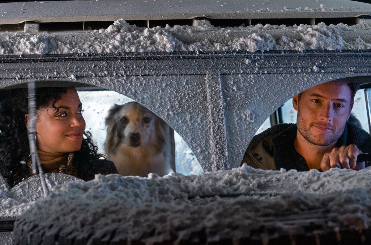 A woman (Barrett Doss) smiles at a man (Justin Hartley) driving a snow-covered car with a dog in the backseat.