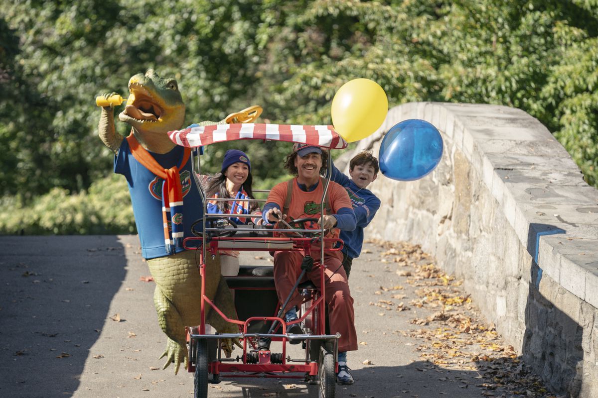 Lyle rides on surrey with Constance Wu, Javier bardem, and some cheering brown-haired kid holding balloons through Central Park