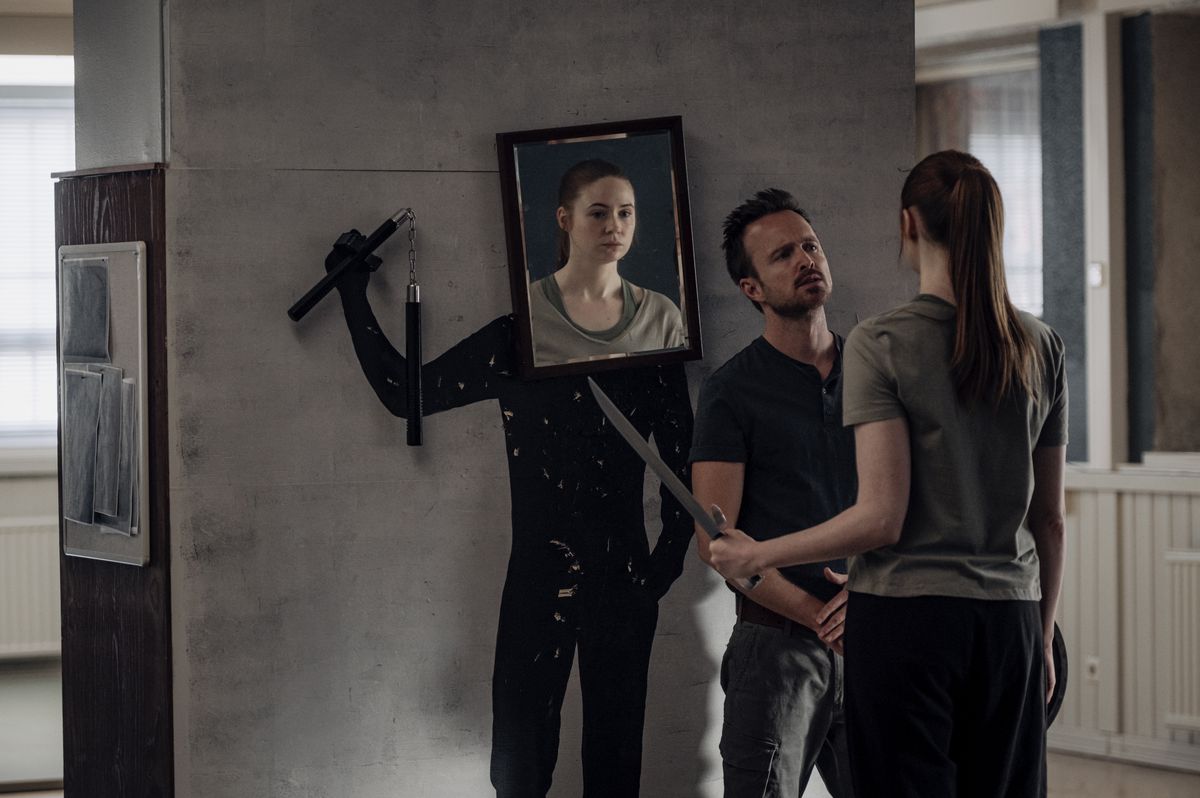 Aaron Paul has Karen Gillan, wielding a katana, face off against a cutout with a photo of her face attached to it, wielding nunchucks, in Dual