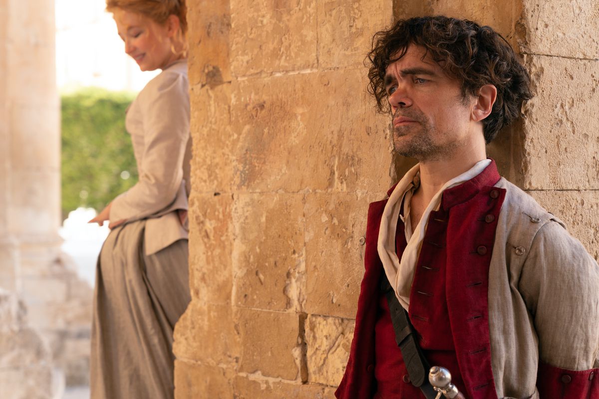 Haley Bennett as Roxanne smiles on the other side of a stone pillar from Peter Dinklage as Cyrano in Joe Wright’s Cyrano