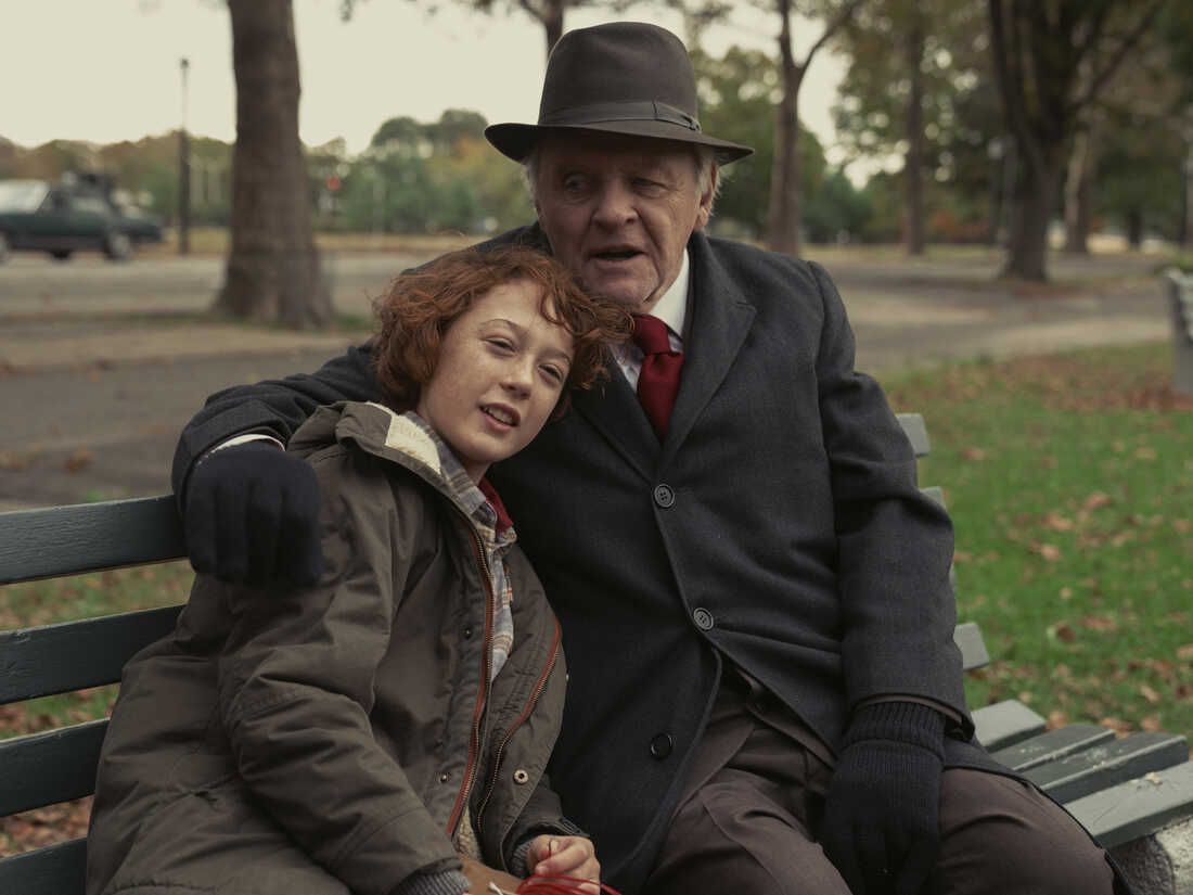 A young boy in a brown coat (Michael Banks Repta) sits on a bench in a park beside an older man (Anthony Hopkins), leaning into a hug.