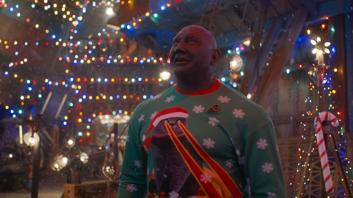Dave Bautista as Draxx smiles surrounded by Christmas lights while wearing a Christmas sweater depicting a cat with laser eyes.
