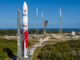 A white, red and gray rocket rolls to an oceanfront launchpad.